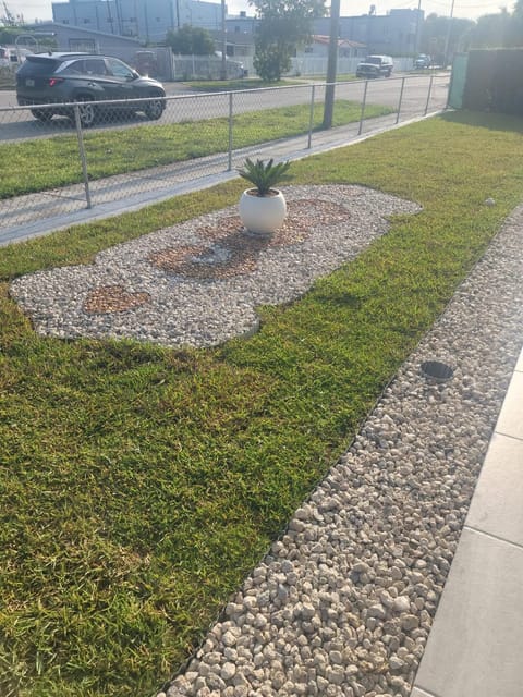 Scrolled pebble mosaic with a sago palm urn along a lawn verge, river rock beside the sidewalk